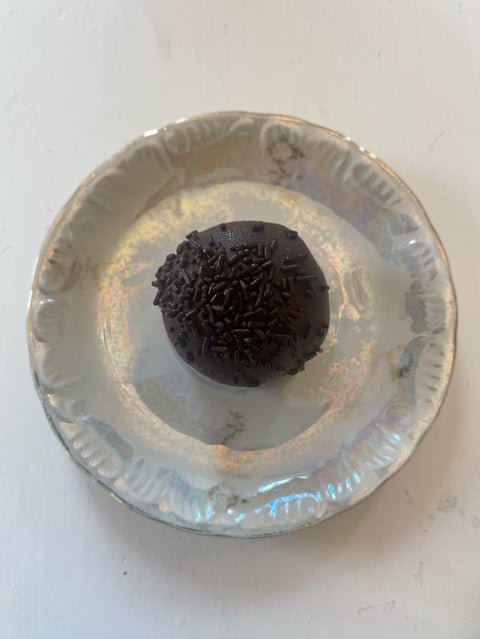 Black chocolate cake ball with sprinkles centered in a white disposable plate