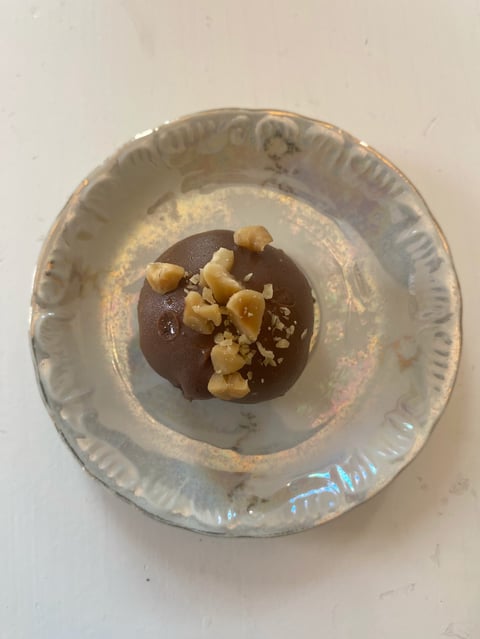 Dark chocolate dessert topped with caramel or toffee pieces on a white disposable plate