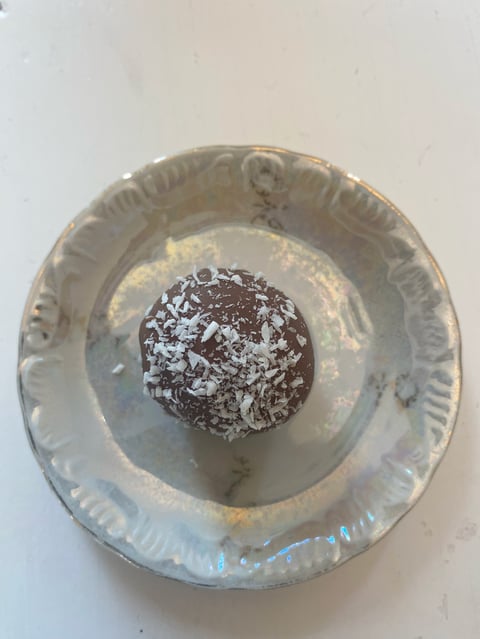 Chocolate ball dusted with coconut on white paper plate against light background