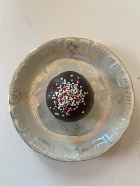 Chocolate sphere topped with colorful pearls sitting in a weathered silver pie dish on white background