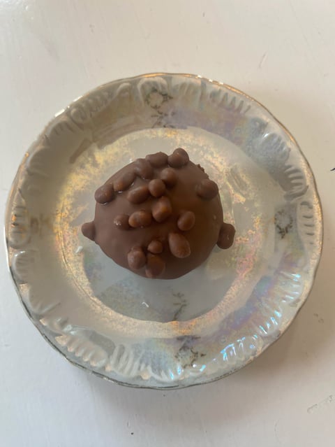 Chocolate candy with cocoa nibs on top placed in center of aluminum foil container on white surface